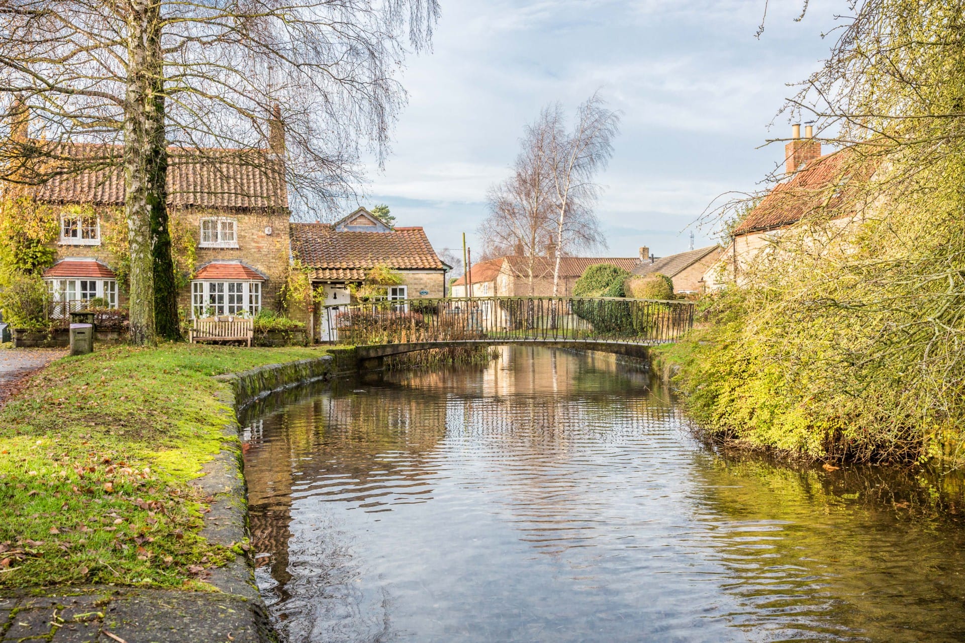 Nettleham village stream with bridge crossing the water. Showing greenery and trees bordering the waters edge